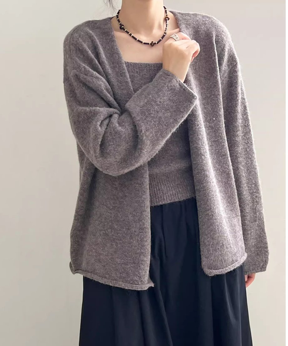 ダークグレーのニットキャミソールのアンサンブルを着用した女性の半身像。黒いロングスカートと太めのネックレスを着用。
