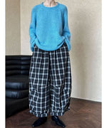 ブルーのローゲージニットと黒白チェックのワイドパンツを着用し、黒い靴を履いた全身写真。ラグランスリーブとざっくりとした編み地が特徴。