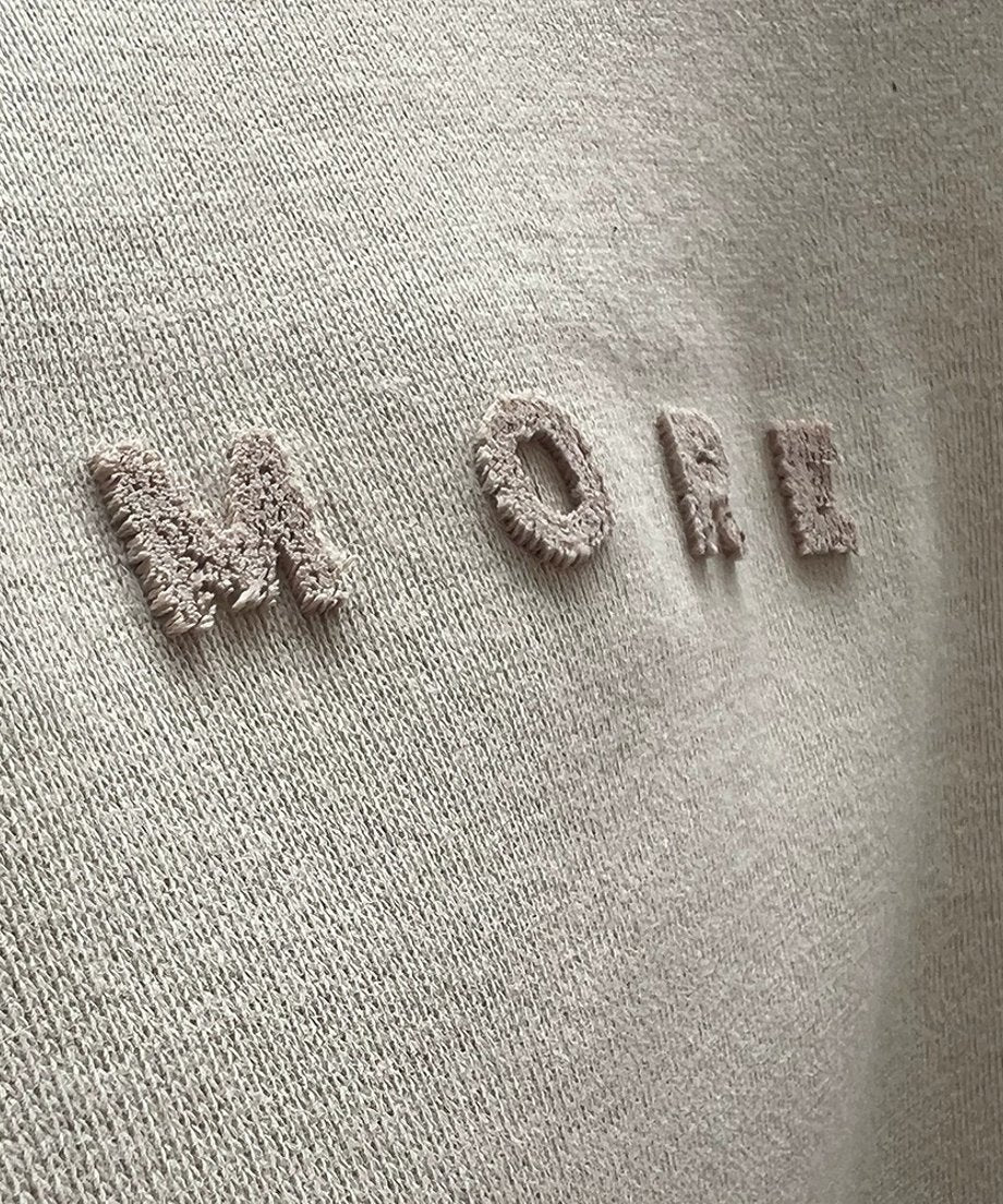 アプリコットのスウェットシャツに施された「MORE」のエンボス加工ロゴのクローズアップ。