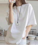 オフホワイトのTシャツを着た女性が飲み物を飲んでいる様子。