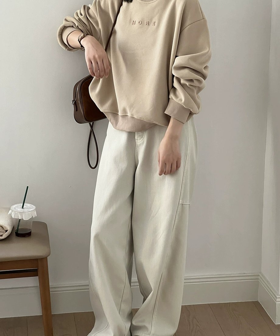 アプリコットのスウェットシャツと白いパンツをコーディネートした女性の全身ショット。