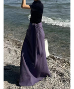 海辺でパープルのラップスカートを着用した女性が黒いトップスと合わせている後姿。