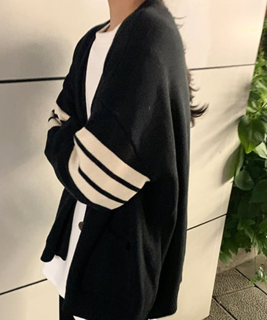 黒いライン入りオーバーサイズカーディガンを横向きで着用し、白いTシャツと合わせた写真。