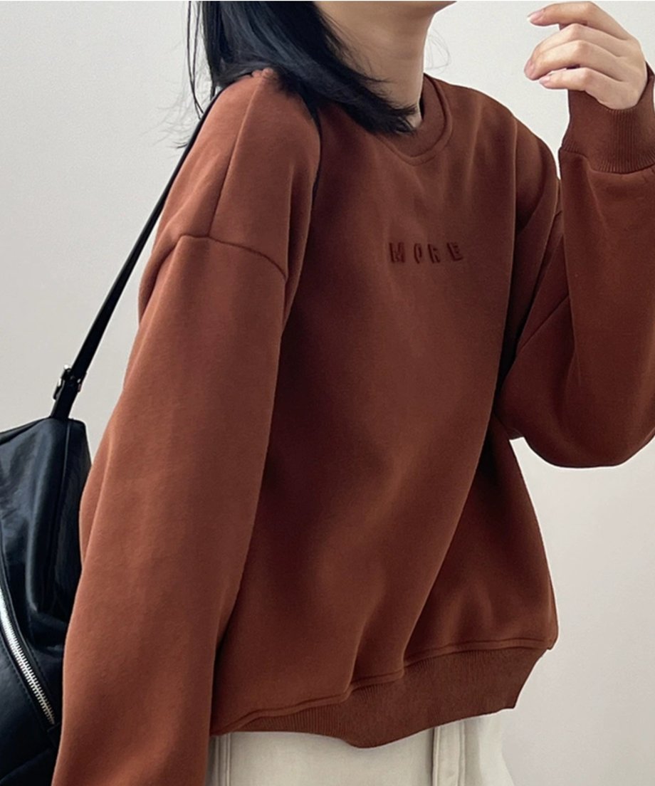 のエンボス加工スウェットシャツとベージュのパンツを着用した女性の半身ショット。