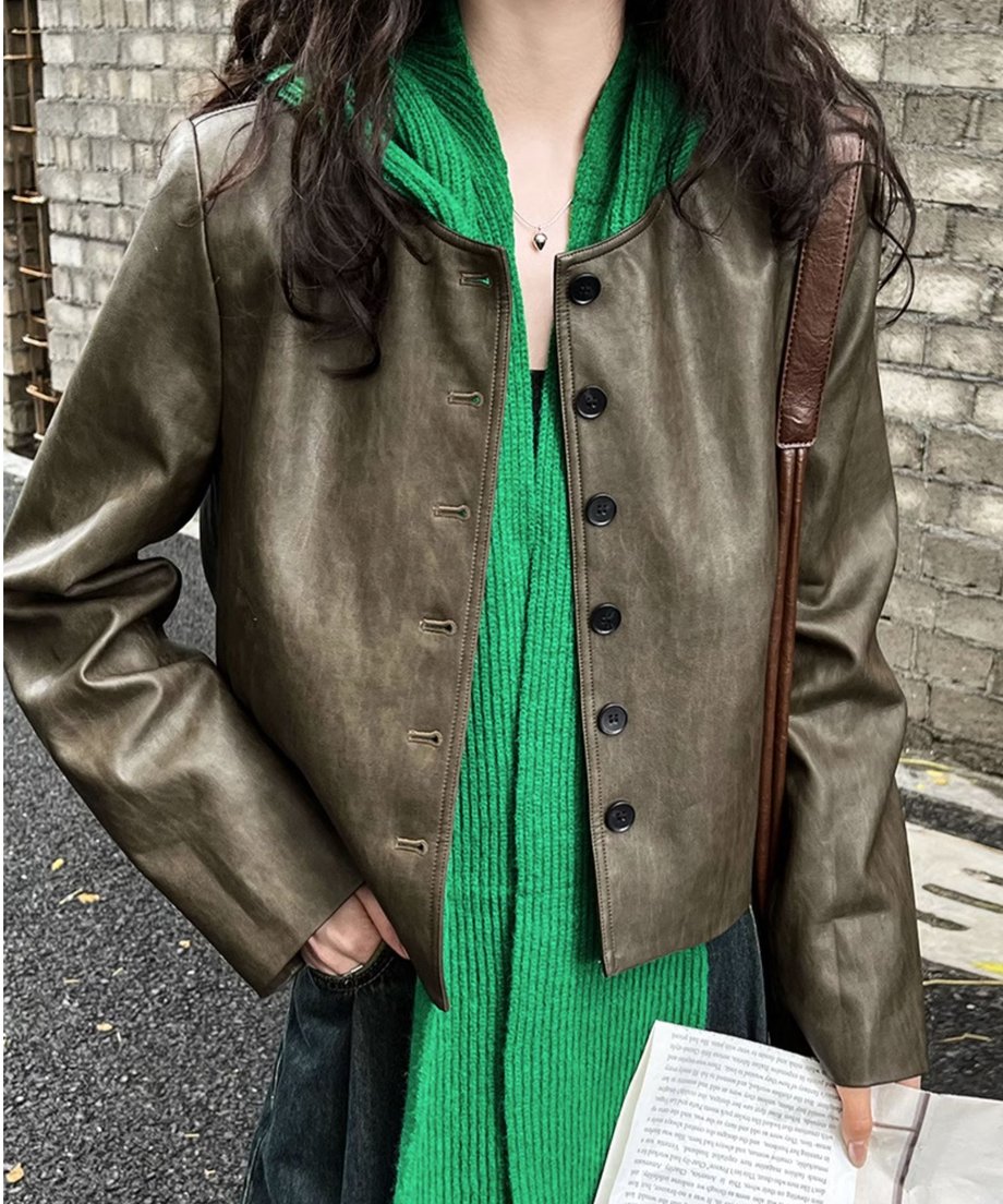 カーキのフェイクレザージャケットを着用した女性のバストアップ。内側に鮮やかな緑色のニットマフラーを巻いている。