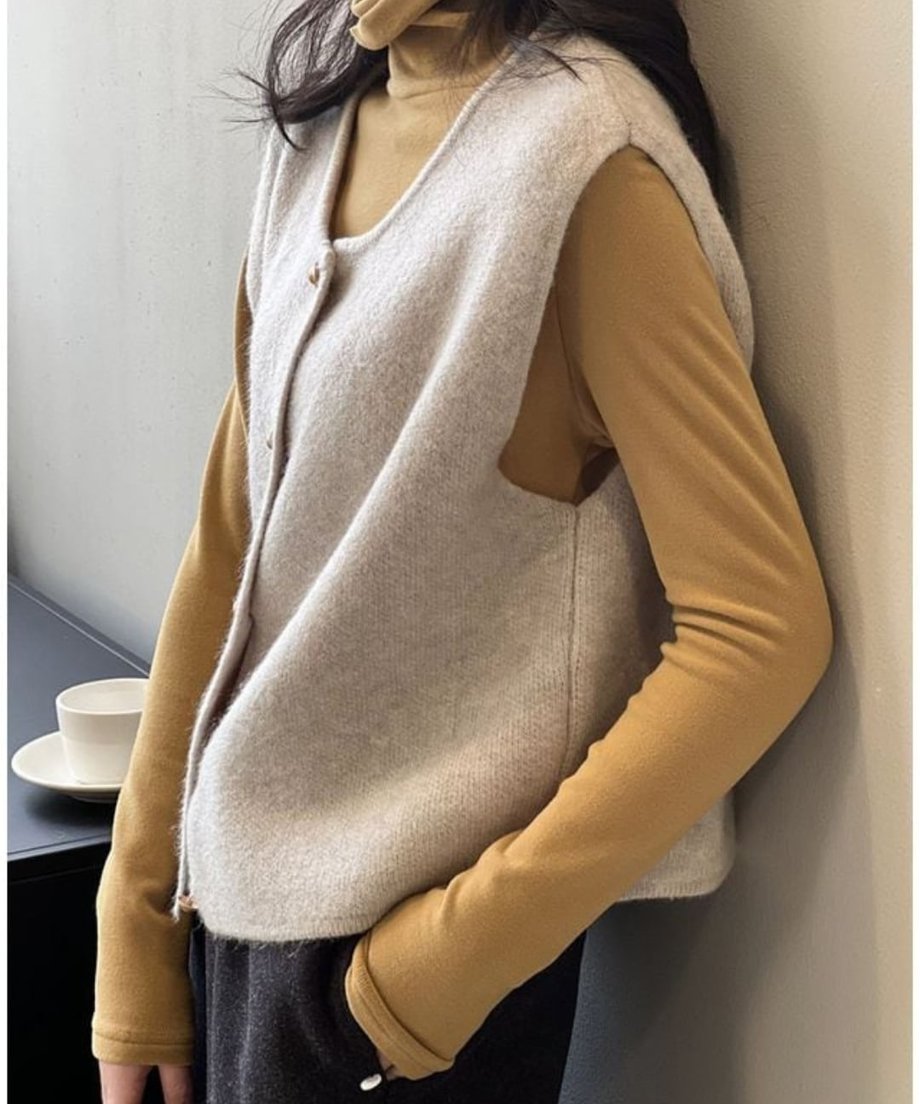 オフホワイトのニットベストを、マスタードイエローのタートルネックトップスに重ね着した女性のクローズアップ。