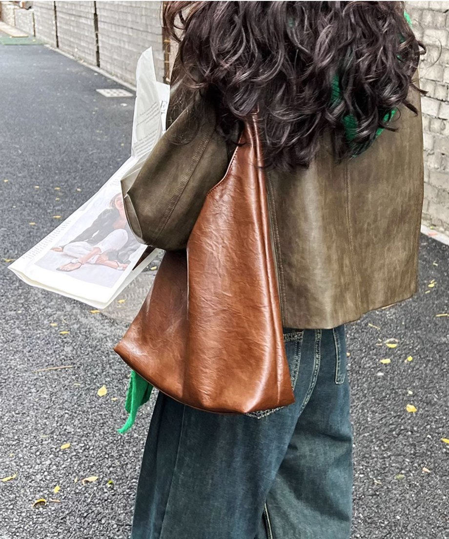 カーキのフェイクレザージャケットを着用した女性の背面。茶色の大きなレザートートバッグと、濃紺のワイドデニムを合わせている。