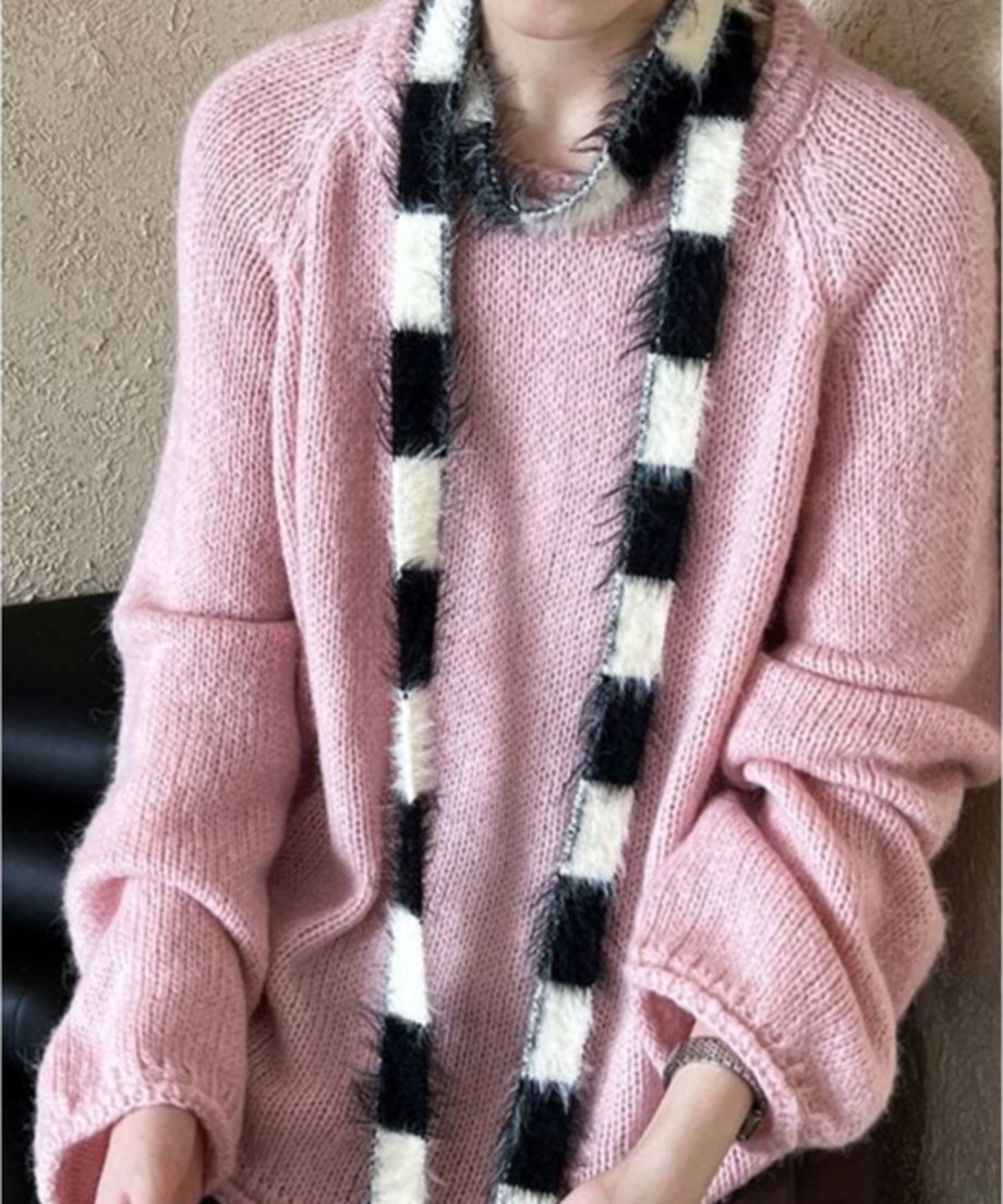 ピンクのローゲージニットを着用し、黒と白のボーダー柄のファーのようなスカーフを首からかけた女性のバストアップ写真。