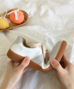 手で大きく曲げられ、柔軟性を示しているグレーのスニーカー。茶色のガムソールが特徴的。