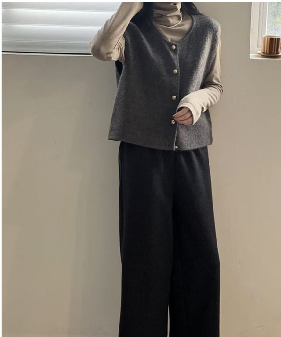 グレーのニットベストに、ベージュのタートルネックトップスと黒のワイドパンツを合わせた女性の全身ショット。