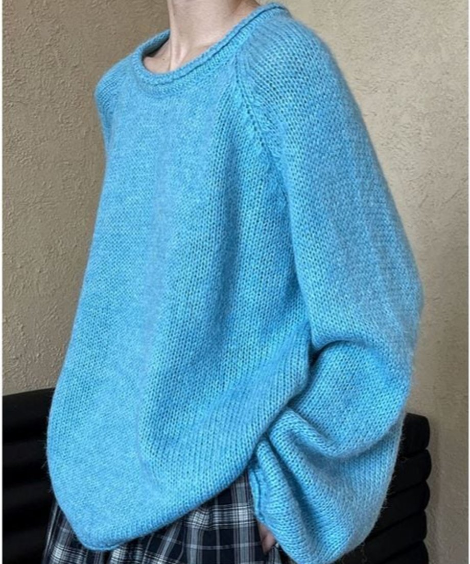 ブルーのローゲージニットを着用した女性の側面からの写真。チェック柄のボトムスが見え、リラックス感のあるシルエットが強調されている。