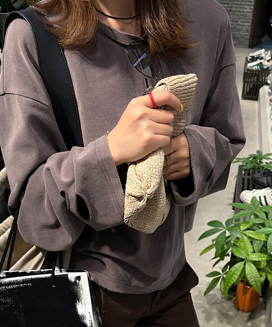 グレーブラウンのダメージ加工プルオーバーに、ベージュの小物を合わせた、素材感のコントラストがわかる手元のクローズアップ。