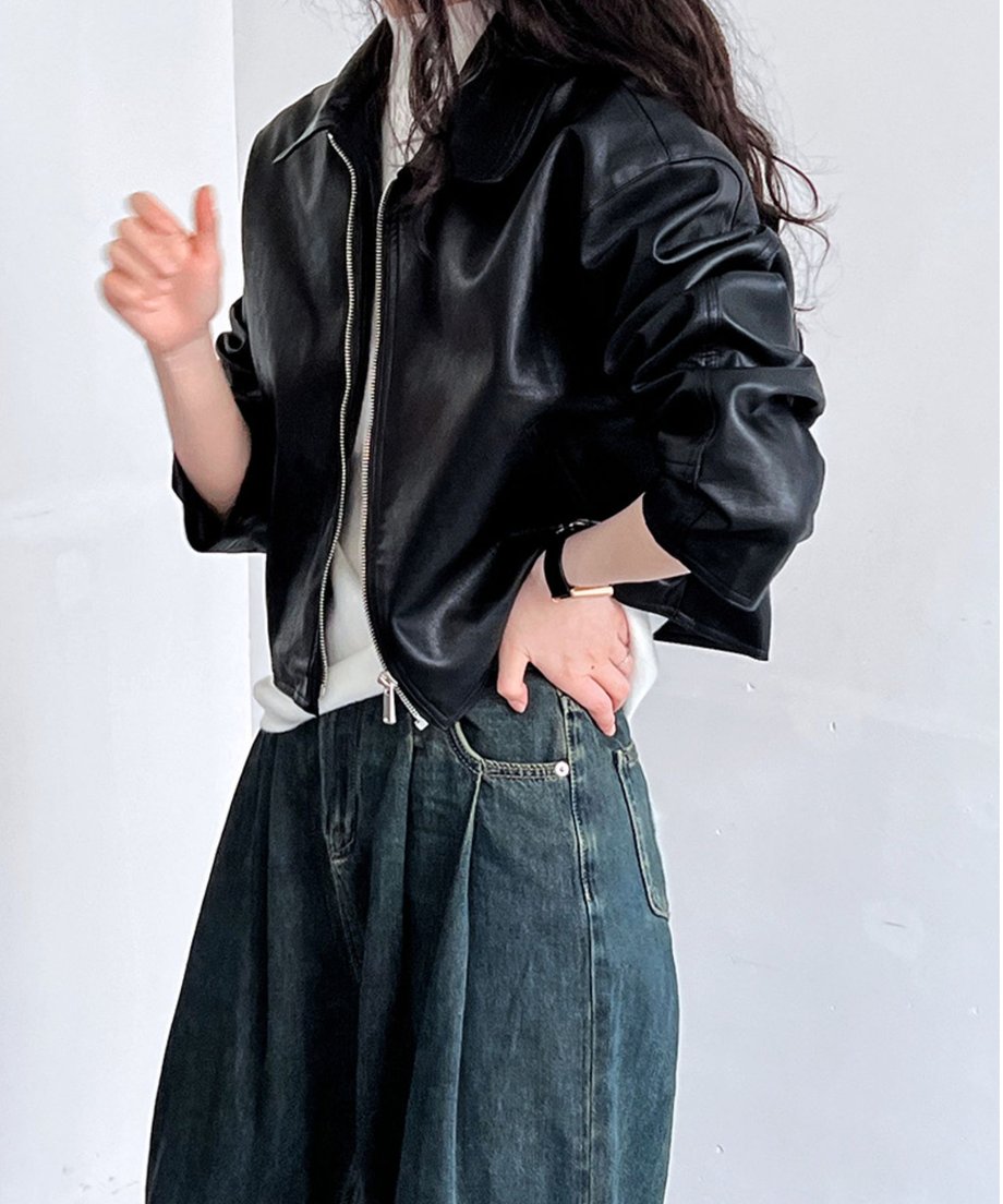黒のクロップド丈フェイクレザーブルゾンを着用した女性が、白のTシャツと濃いインディゴのワイドデニムに合わせ、横を向いているショット。