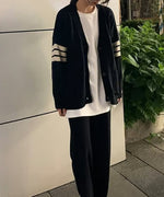 黒いライン入りオーバーサイズカーディガンを正面から着用した人物の全身。白いロングTシャツが裾からのぞいている。