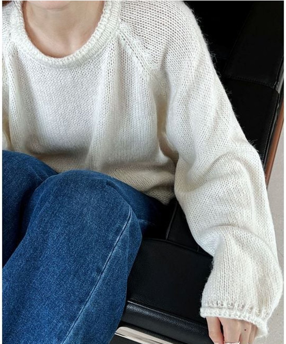 ホワイトのローゲージニットを着用した上半身のクローズアップ。濃い青のデニムパンツを履いており、ゆったりとした袖のシルエットが見える。