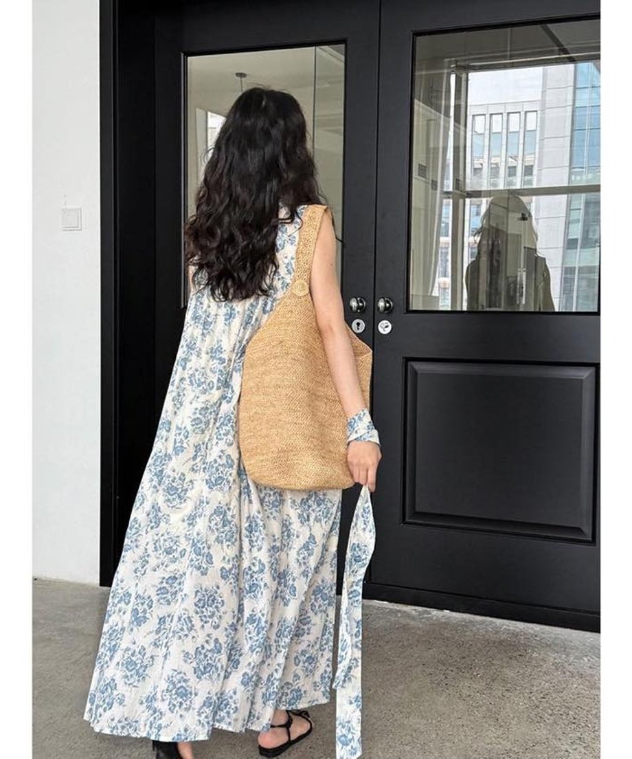 女性がブルーフラワーワンピースを着用し、かごバッグを持って歩いている後ろ姿の写真
