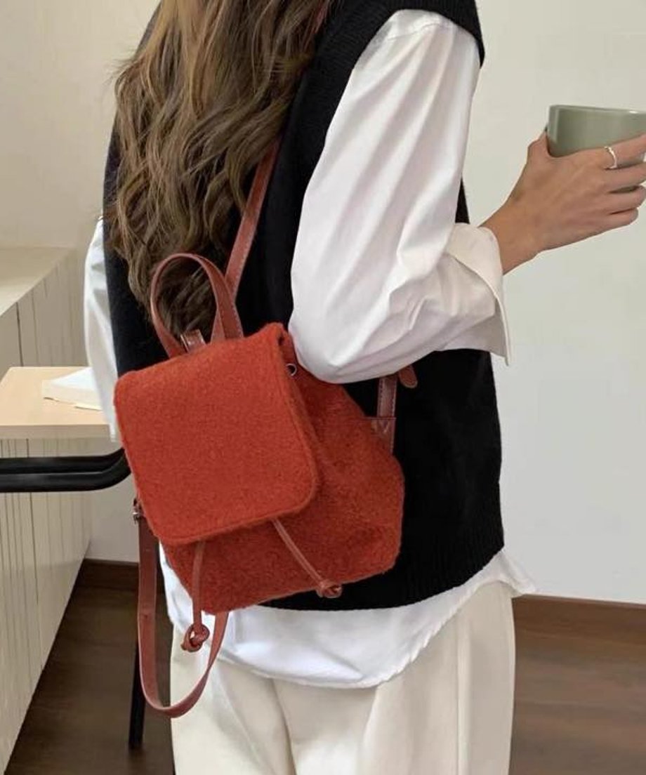 黒のベストと白のシャツ、ベージュのパンツを着用した女性が、赤色のボア素材のミニリュックを背負っている後姿。
