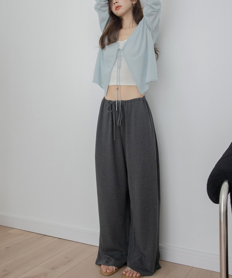 アイスブルーのドロストシアーカーディガンを白のタンクトップとチャコールグレーのワイドスウェットパンツに合わせた女性の全身。両手を上げてリラックスしたポーズ。