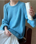 ブルーのローゲージニットを着用し、白いスカートと合わせた女性が椅子に座って本を持っている写真。