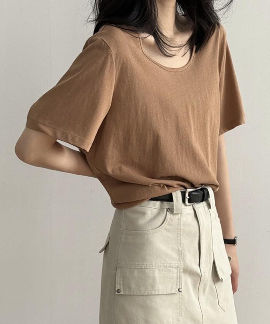 キャメルのUネックTシャツを着用した女性の上半身。Tシャツをベージュのカーゴポケット付きスカートにタックインし、黒いベルトを締めている。