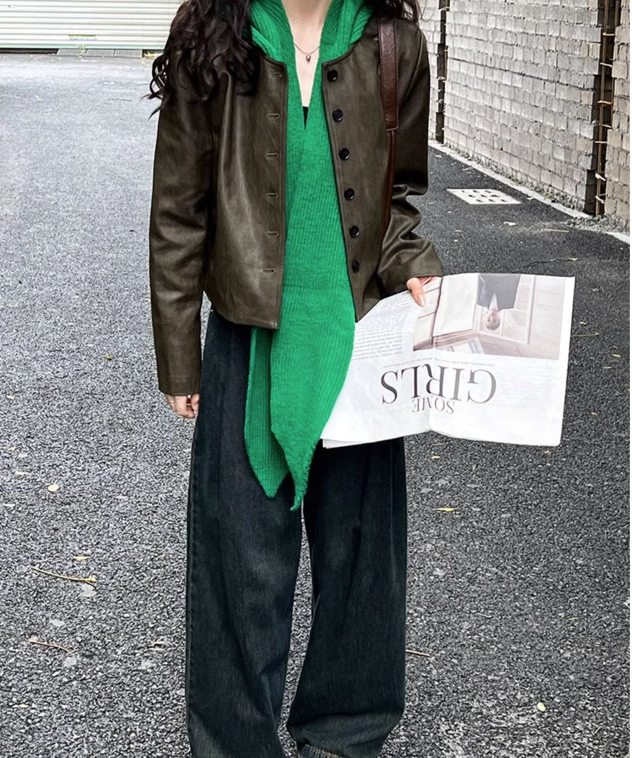 カーキのフェイクレザージャケットに緑のニットを肩掛けした女性の正面ショット。