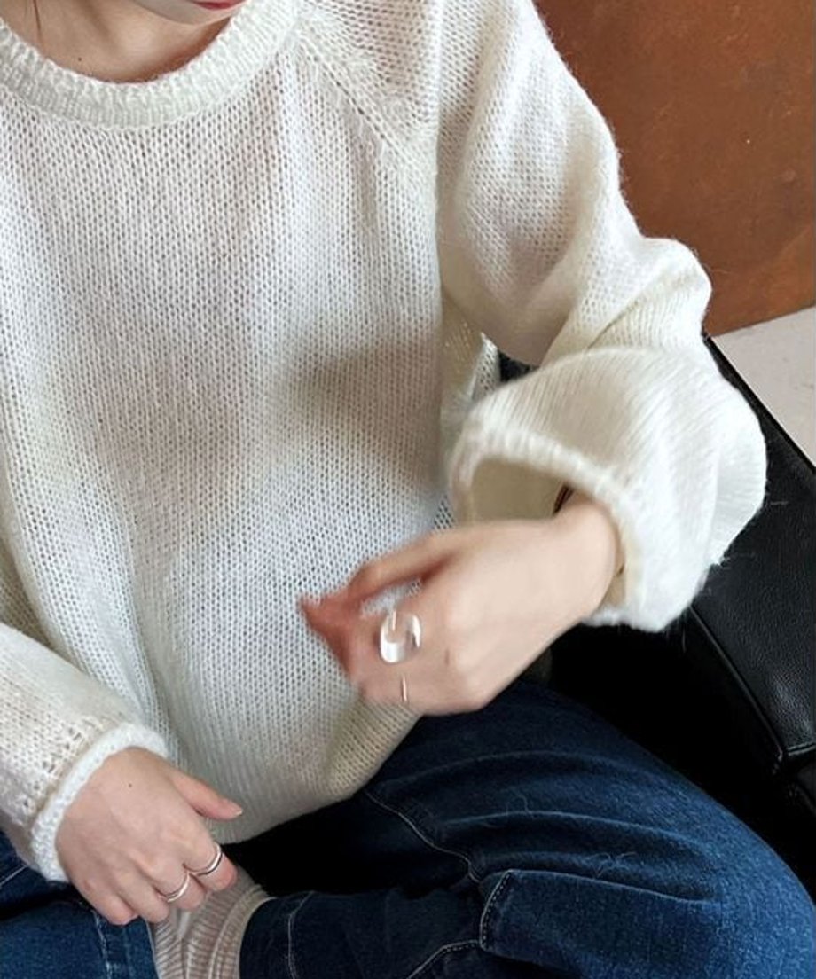 ホワイトのローゲージニットを着用した手元と上半身のクローズアップ。透け感のあるざっくりとした編み地と、バルーンスリーブ風の袖口がわかる。
