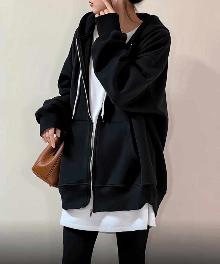 ブラックフーディーと白いトップスを着た女性が、ブラウンのバッグとスニーカーをコーディネート。