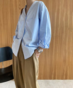カーキのハイウエストタックパンツと水色のビッグシャツのコーディネート。シャツの袖をロールアップし、パンツのポケットに手を入れている。