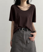 ブラウンのUネックTシャツを着用した女性の上半身。Tシャツをグレーのカーゴポケット付きミニスカートにタックインし、黒いベルトを締めている。