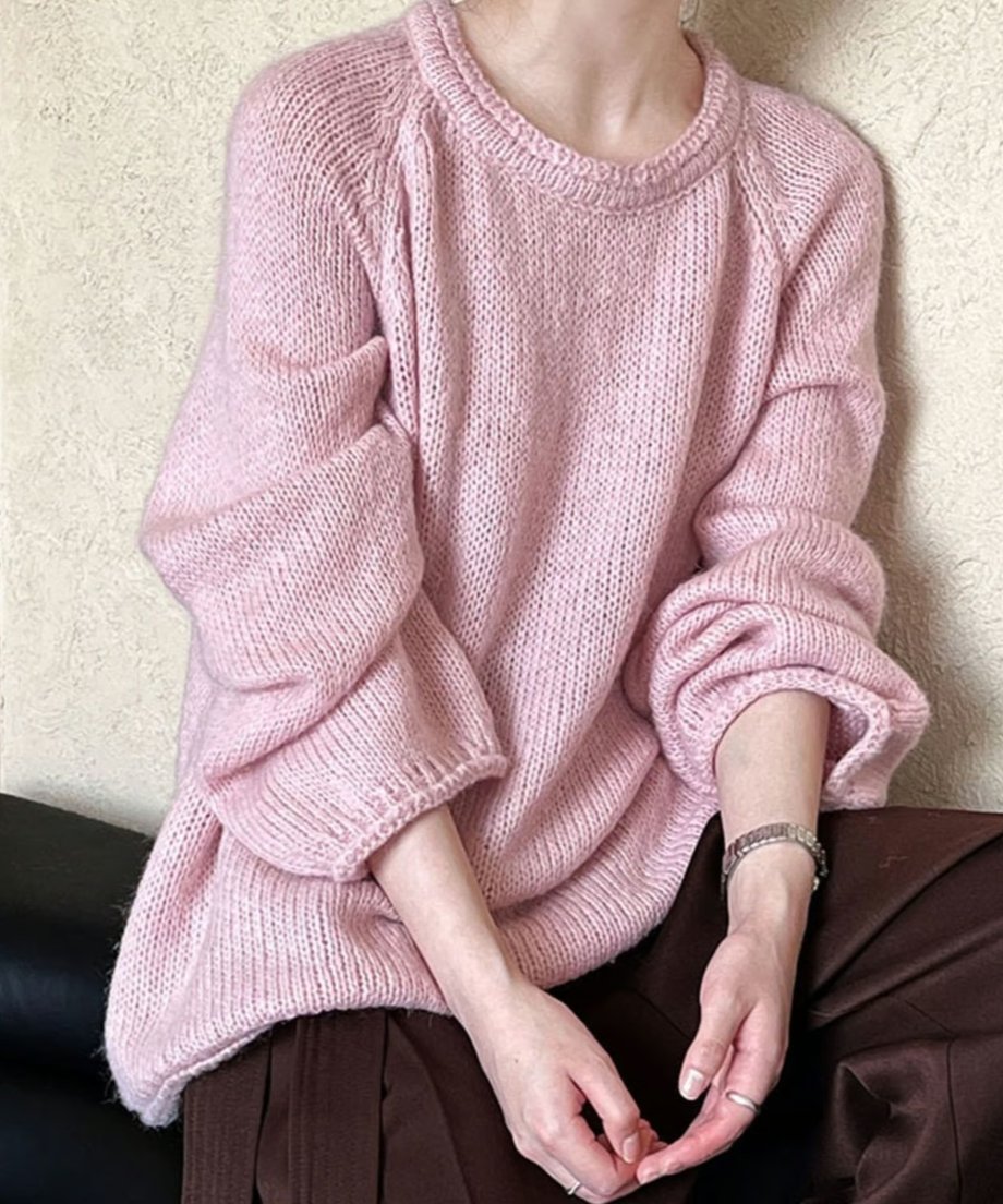 ピンクのローゲージニットを着用し、茶色のボトムスを履いた上半身写真。女性が座っており、アクセサリーが見える。