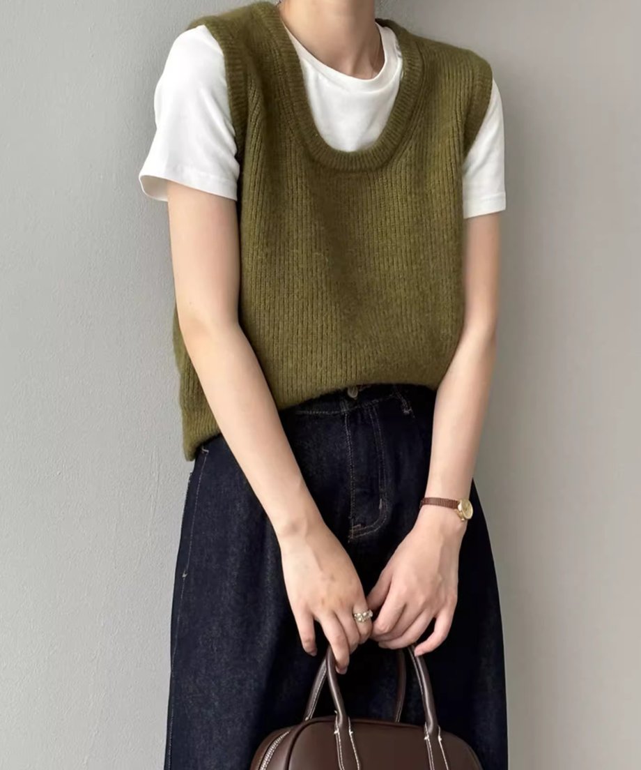 カーキ色のUネックニットベストを白Tシャツと濃い色のデニムにレイヤードして着用している女性の正面ショット。