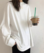 白のオーバーサイズ長袖Tシャツ（カットソー）を着用した女性のクロースアップ。ロング丈でゆったりとしたシルエットが特徴的で、アイスドリンクを持っている。
