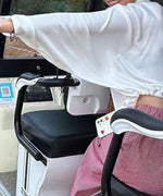 ホワイトのドローストリング薄手シャツの裾をドローストリングで絞り、クロップド丈になった状態で乗り物（バギーのようなもの）の座席に座っている人物。