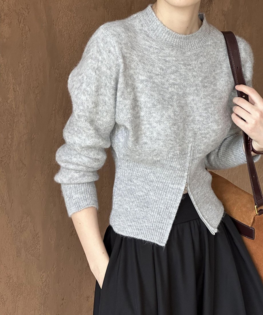 グレーのハーフジップニットと黒いロングスカートを着用した女性の胸元。茶色のスエードバッグを肩に掛けている。