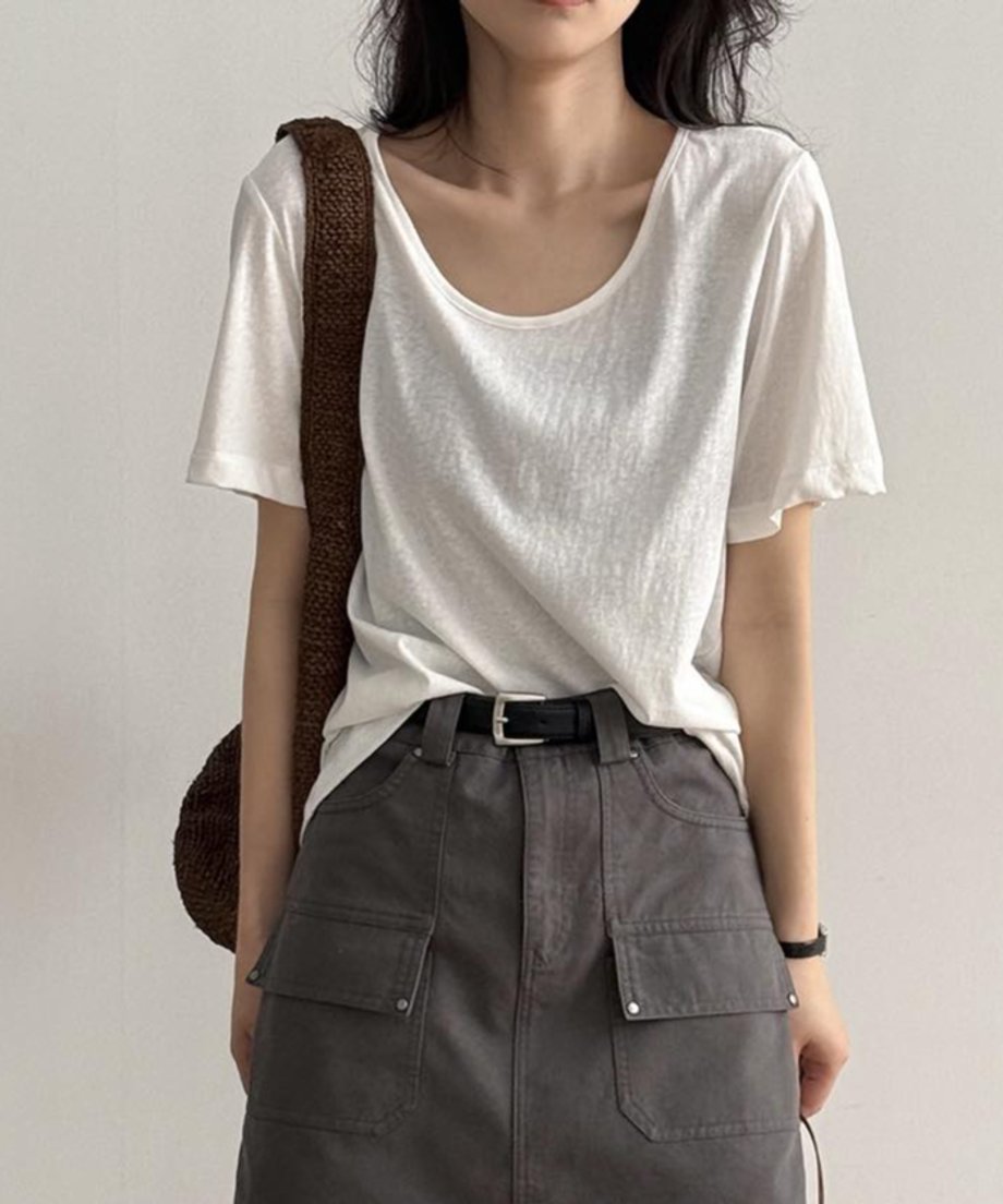 ホワイトのUネックTシャツを着用した女性の上半身。Tシャツをグレーのカーゴポケット付きミニスカートに軽くタックインし、黒いベルトを締めている。