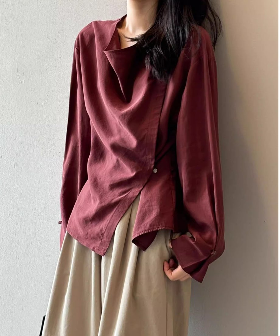 ボルドーのドレープブラウスとベージュのスカートを着用した女性が、リラックスしたポーズをとっている画像。