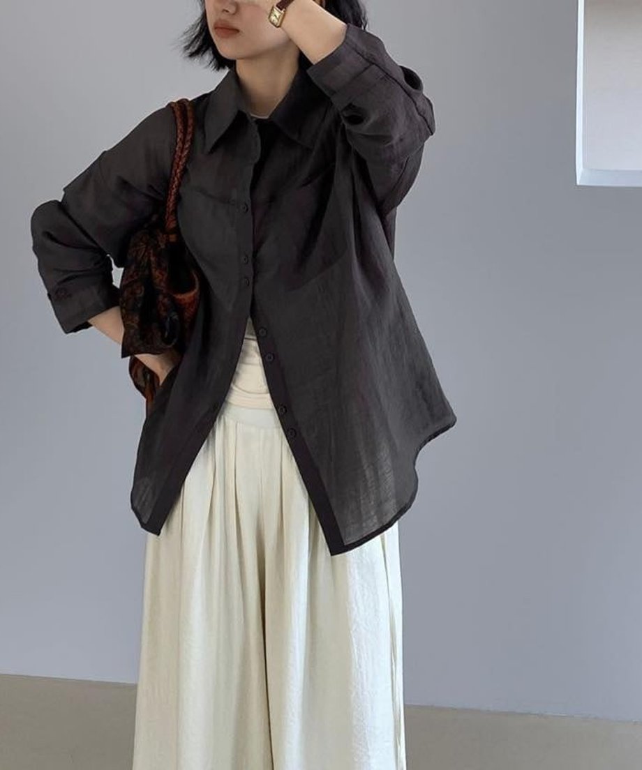 ダークグレーのリボンシアーシャツを羽織り、アイボリーのワイドパンツを合わせた女性の全身画像。茶色のバッグを持っている。