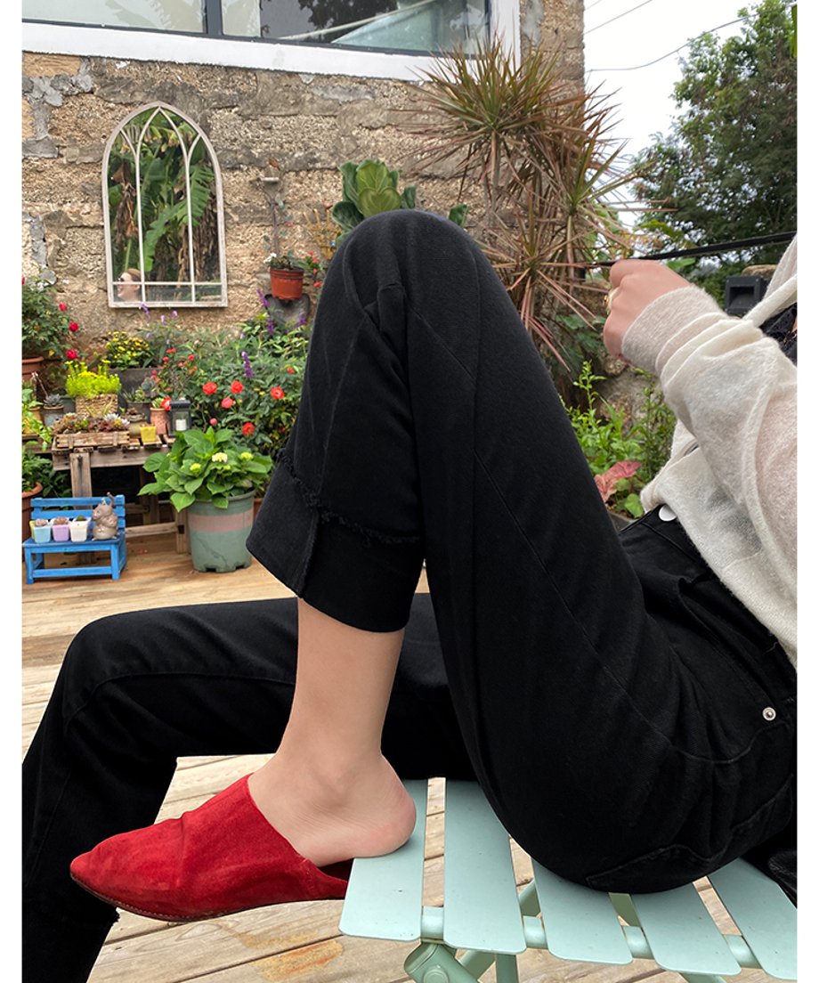 黒の裾カフス付きストレートパンツを着用した女性がベンチに座った写真。白いカーディガンと赤のスエード調ミュールを合わせている。