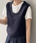 ブラックのUネックニットベストを白Tシャツと濃い色のデニムスカートにレイヤードして着用している女性のクローズアップ。首元にはシルバーのネックレスが見える。