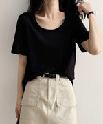 黒色のUネックTシャツを着用した女性の上半身。Tシャツをベージュのパンツにタックインし、黒いベルトを締めている。