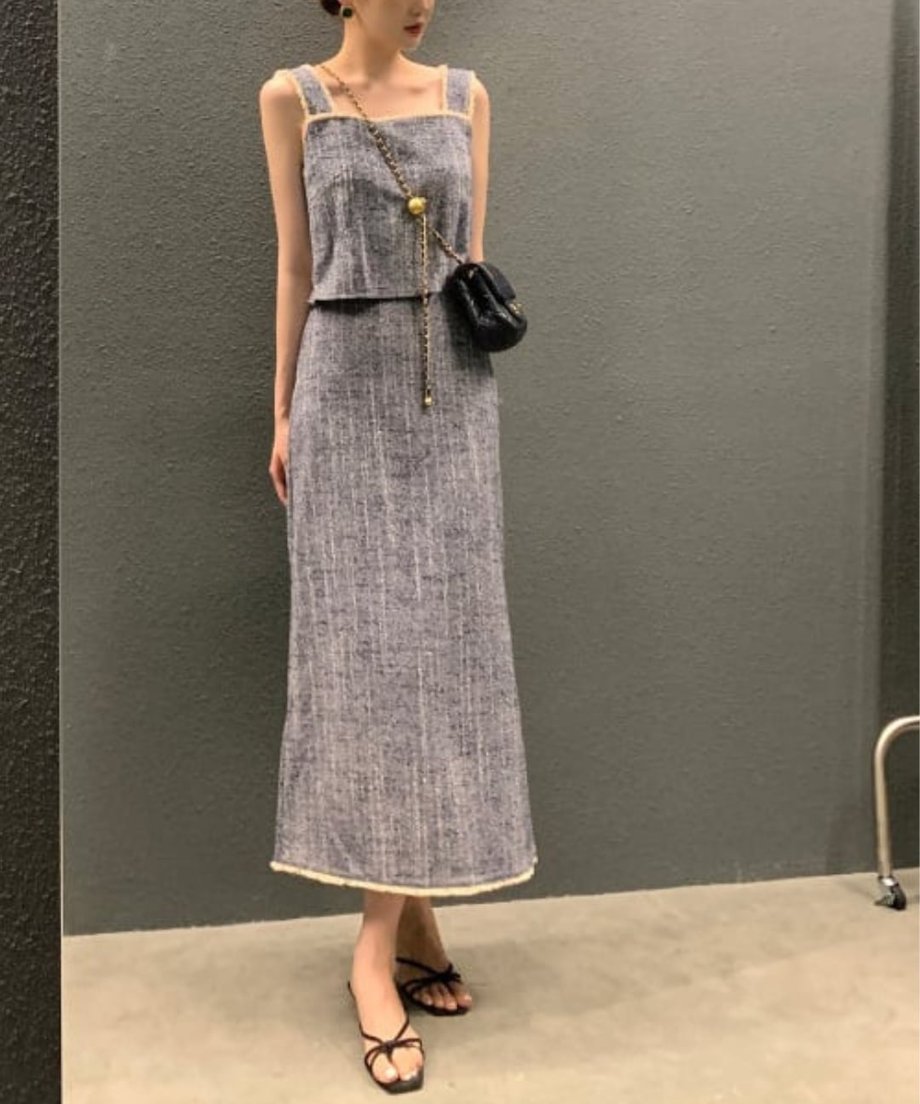 ブルーのツイードセットアップを着用した女性の全身像。黒いチェーンバッグとサンダルを合わせている。
