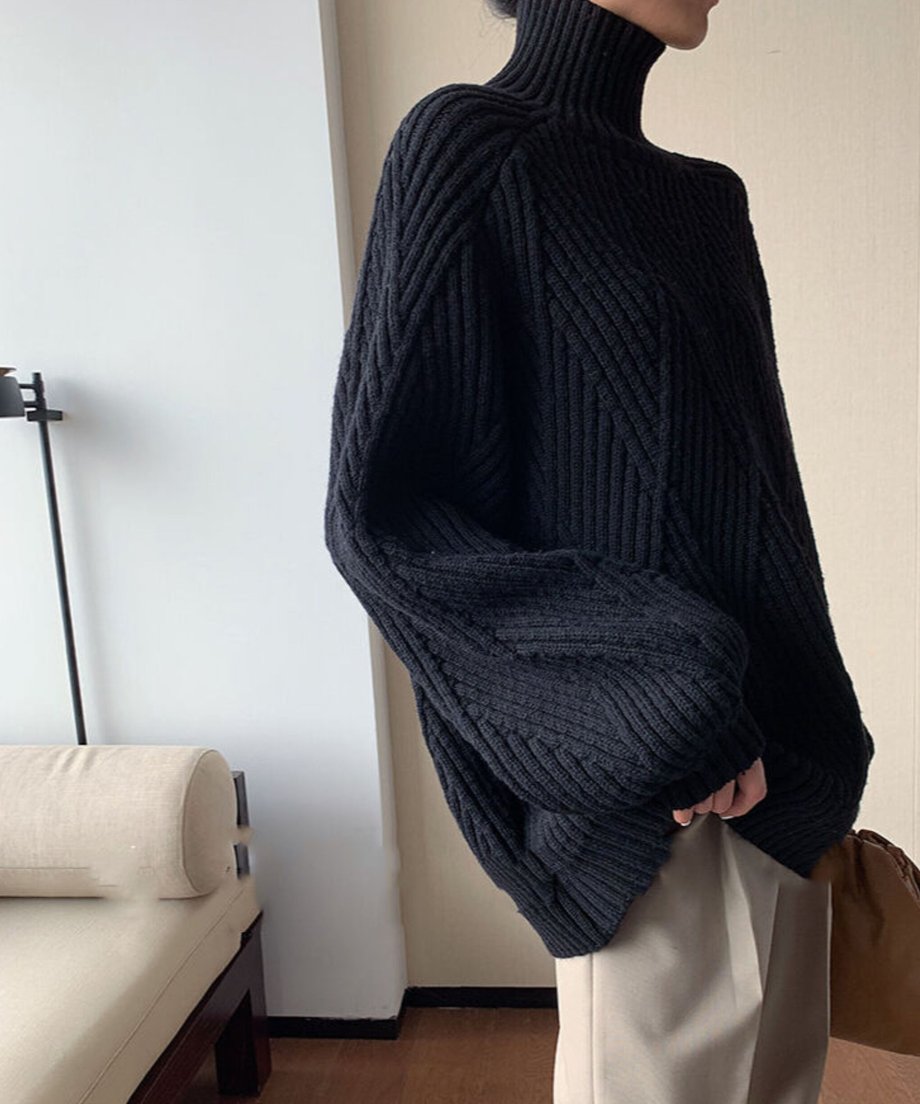 ブラックのオーバーサイズニットセーターを着た人物がベージュのパンツとコーディネートしている。