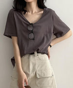 ダークグレーのVネックTシャツを着用し、眼鏡を下げた女性の上半身。Tシャツをベージュのカーゴポケット付きスカートにタックインし、黒いベルトを締めている。