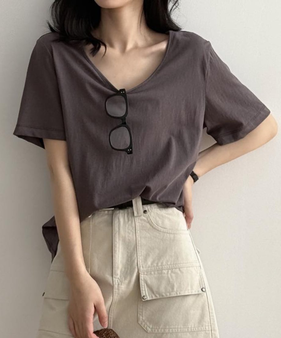 ダークグレーのVネックTシャツを着用し、眼鏡を下げた女性の上半身。Tシャツをベージュのカーゴポケット付きスカートにタックインし、黒いベルトを締めている。
