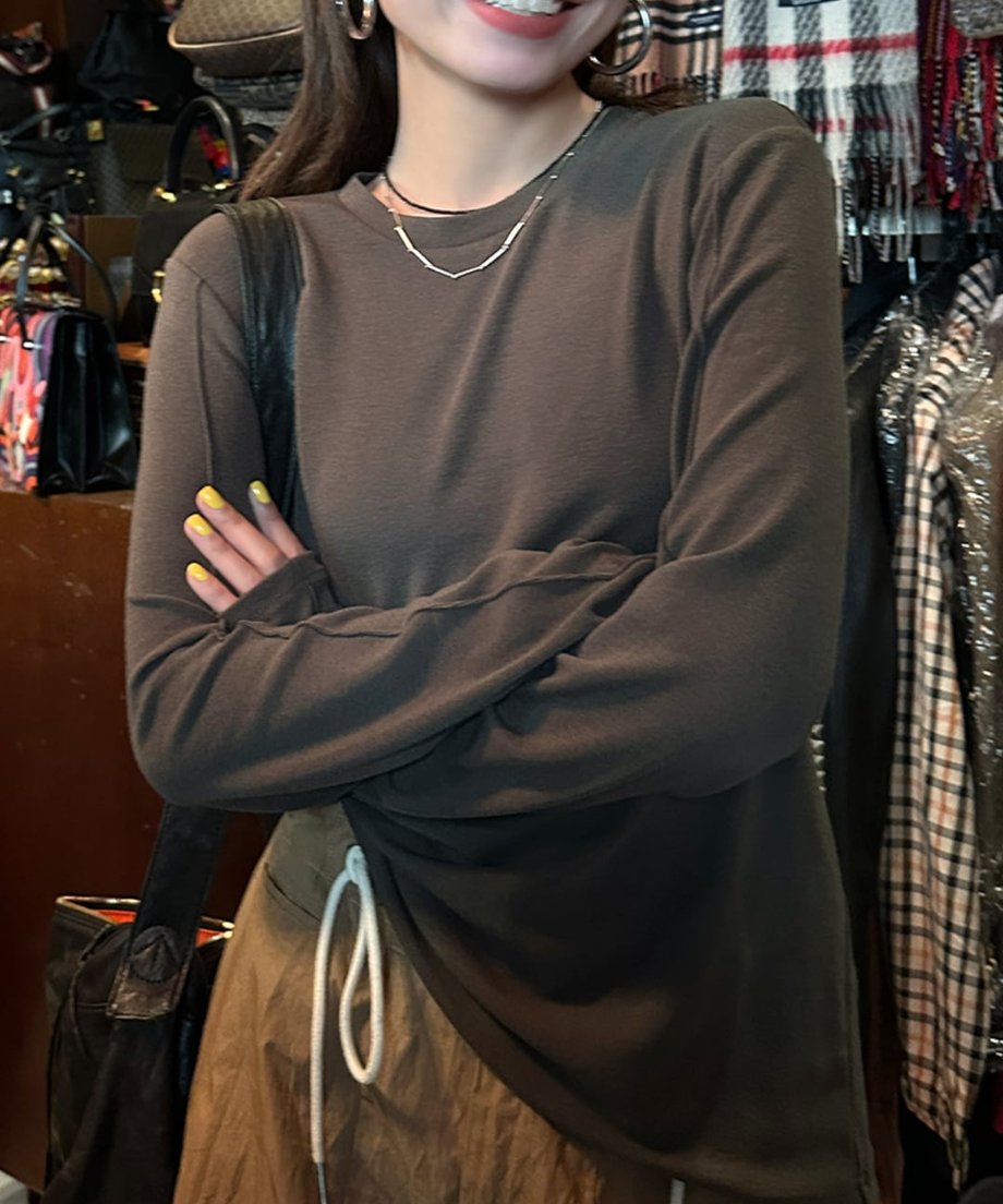 グレーのアウトシームロングTシャツを着た人物が腕を組んで立っている上半身。右側から左側へ斜めに入った縫い目が特徴的。