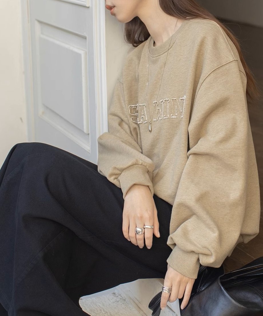 ベージュのロゴスウェットシャツを着た女性が座ってリラックスしている。