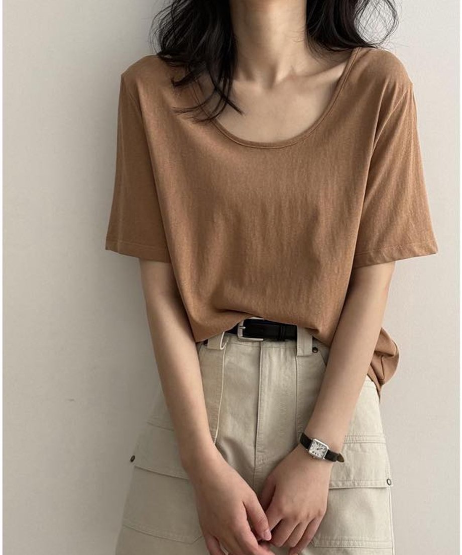 キャメルのUネックTシャツを着用した女性の上半身。Tシャツをベージュのカーゴポケット付きスカートにタックインし、黒いベルトを締めている。