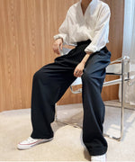 ブラックのハイウエストワイドタックパンツを白いシャツに合わせたコーディネートで椅子に座る女性。パンツのゆったりとしたシルエット。
