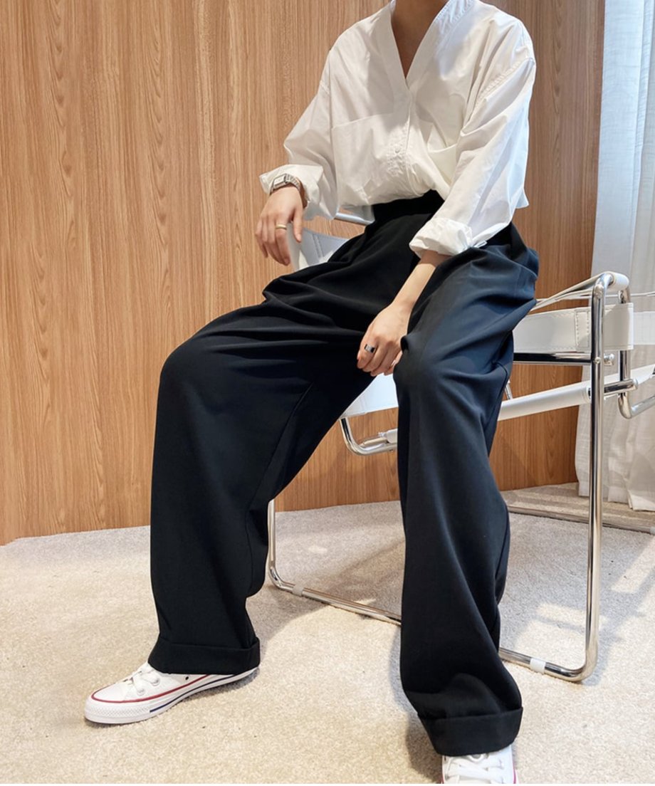 ブラックのハイウエストワイドタックパンツを白いシャツに合わせたコーディネートで椅子に座る女性。パンツのゆったりとしたシルエット。
