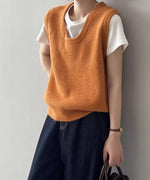 オレンジ色のUネックニットベストを白Tシャツと濃い色のワイドデニムにレイヤードし着用している女性の全身ショット。